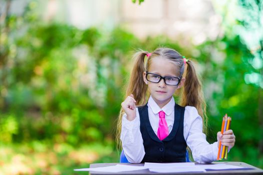 Adorable little school girl at desk with notes and pencils outdoor. Back to school.