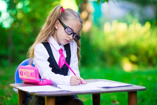 Adorable little school girl at desk with notes and pencils outdoor. Back to school.