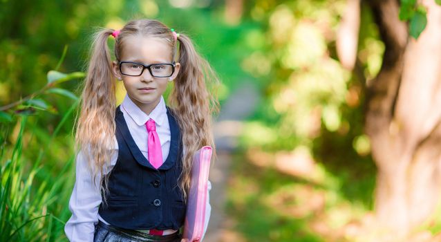 Portrait of adorable little school girl with notes in glasses outdoor going to school