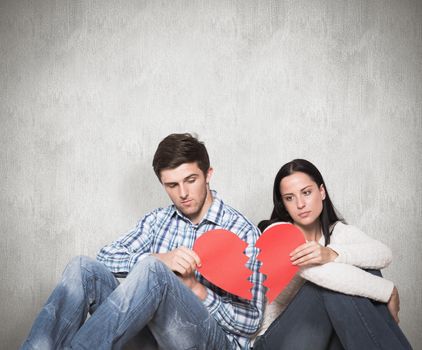 Composite image of young couple sitting on floor with broken heart
