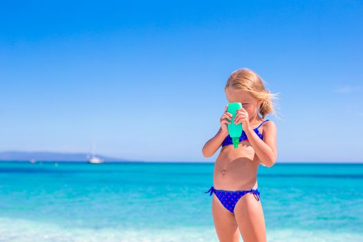 Little adorable girl with suntan lotion bottle on the beach