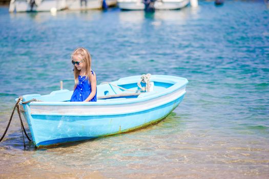Cute girl in blue boat in the sea bay near the town of Mykonos in Greece. Little kid enjoy swimming in the small boat.