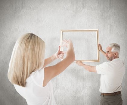 Composite image of couple hanging a frame together