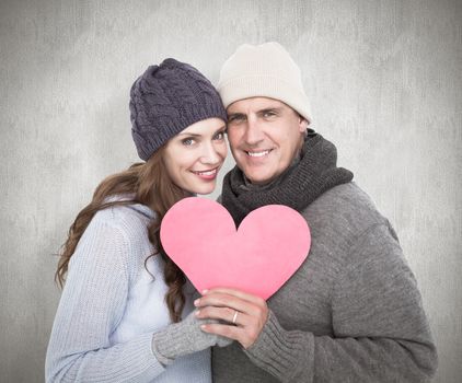 Happy couple in warm clothing holding heart against white background