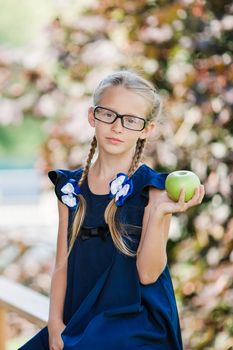 Adorable little school girl with green apple outdoor. Back to school concept