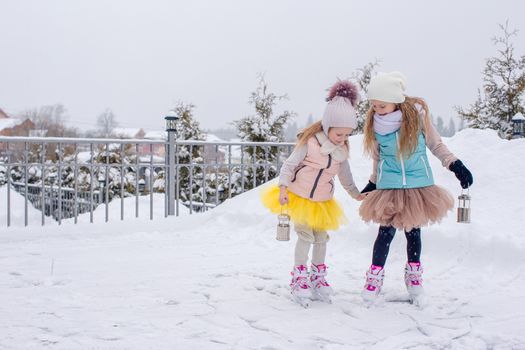 Adorable girls skating on ice rink outdoors in winter snow day
