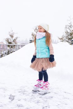 Adorable girl skating on ice rink outdoors in winter snow day