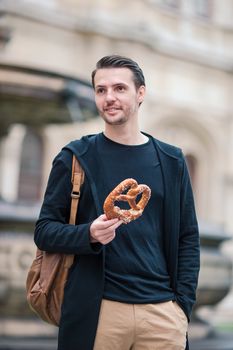 Beautiful young man holding pretzel and relaxing in park