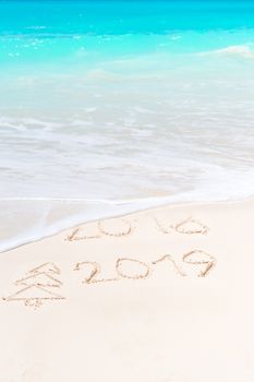 2018 and 2019 handwritten on sandy beach with soft ocean wave on background