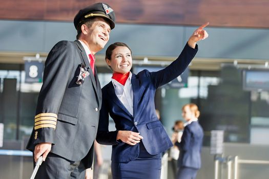 Young attractive stewardess pointing aircraft with the pilot in airport
