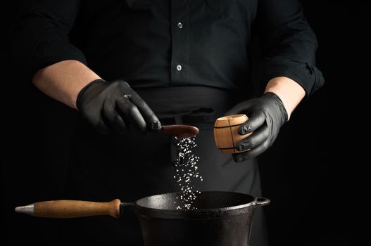 male cook in black uniform and latex gloves salt food in a black