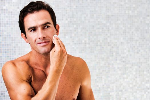Portrait of young attractive man cleansing his face with cotton and toner in the bathroom
