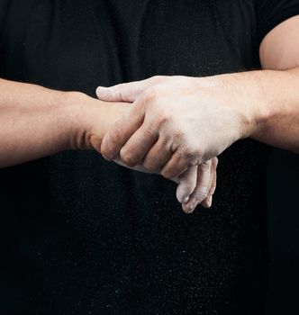 muscular athlete in a black uniform rubs his hands with white dr