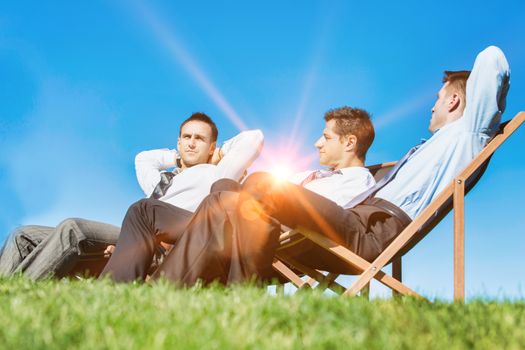Group of handsome businessmen relaxing and talking about life while sitting on folding chair at park