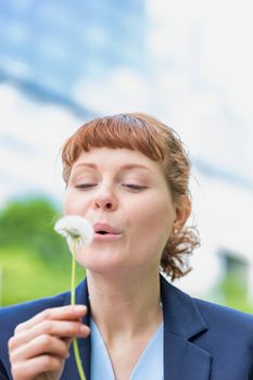 Portrait of young attractive businesswoman wishing on dandelion