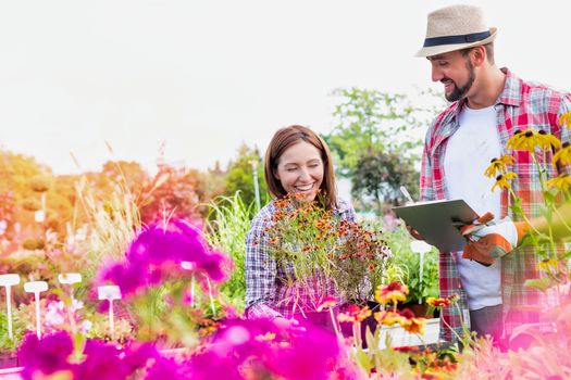 Portrait of mature gardener writing report on clipboard over flowers in shop with woman buyer