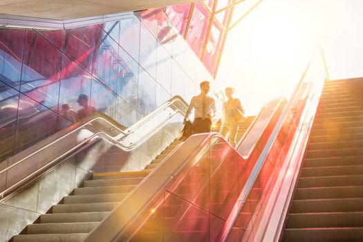 Businessman and businesswoman talking while walking down stairs with lens flare in background