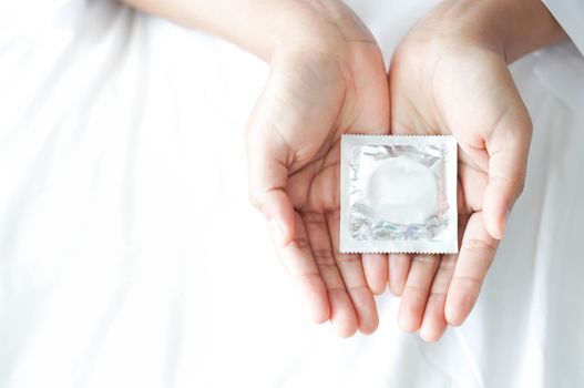 Close up woman hand holding condom lying on white bed, health ca