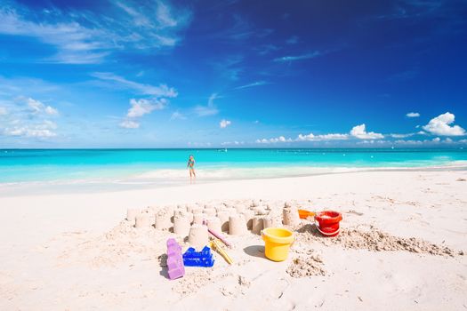 Sandcastle at white sandy beach with plastic kids toys and sea background