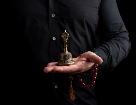 adult man in a black shirt holds a copper Tibetan ritual bell, l