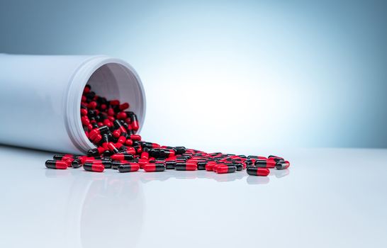 Red-black antibiotic capsule pills spread out of white plastic d