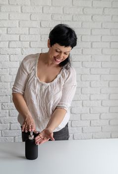 Positive middle aged woman using sanitizing gel to clean hands