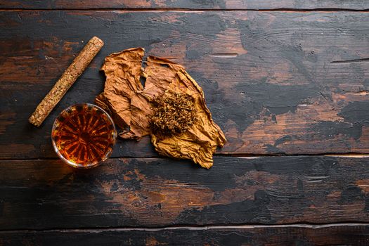 Dried tobacco leave and cut tobacco with cigar and whiskey rum on wood background on vintage dark table. top view space for text