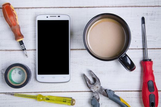 smartphone, coffee cup and equipment repair on the white wooden 