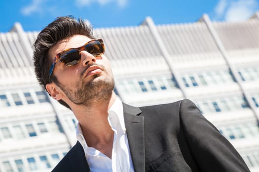 Confident handsome man with sunglasses standing outdoor, building behind his.