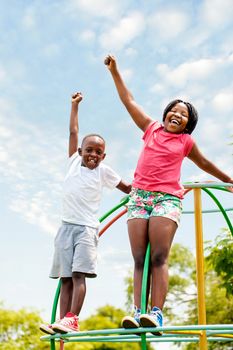 Full length portrait of two African kids shouting and raising hands in park.