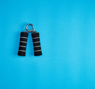 black sports expander for rocking arm muscles on a blue background, copy space