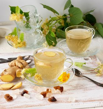 transparent cup of herbal linden tea and pieces of ginger on a w