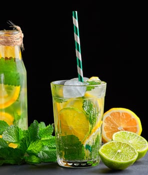 refreshing drink lemonade with lemons, mint leaves, ice cubes and lime in a glass on a black background, copy space