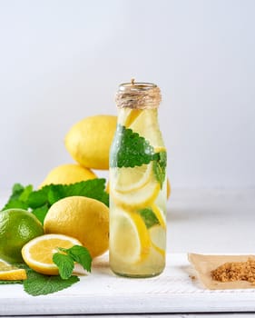 summer refreshing drink lemonade with lemons, mint leaves, lime in a glass bottle, next to the ingredients for making a cocktail