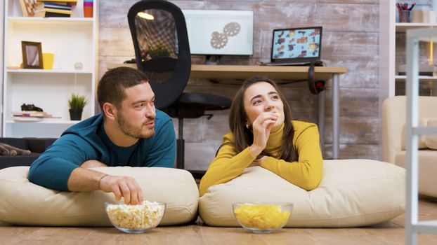Cheerful couple watching tv sitting on pillows