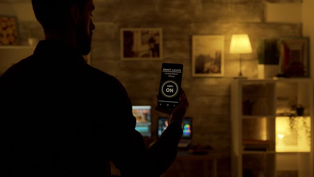 Man uses voice activated smart lights app on his smartphone to tun on the lights in the house
