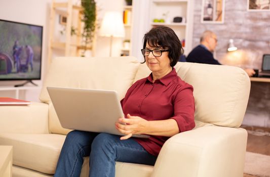 Elderly woman in her 60s sitting on the couch using a laptop