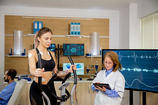 Female athlete running tests on the stepper and doctor making notes in tablet