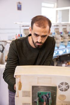 Young worker from the textile factory who controls an embroidery machine