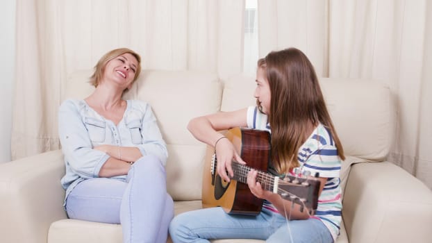 Teenage girl plays a song on the guitar to her mother