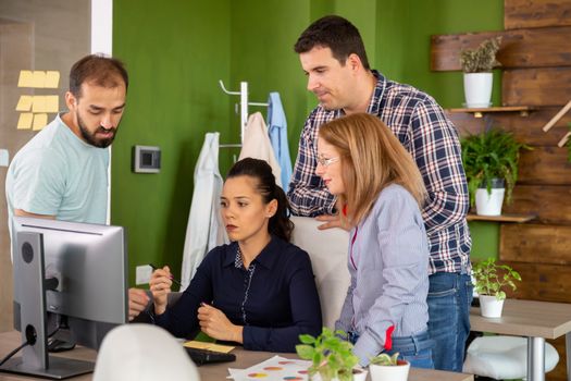 Team of people in start-up office talking at a colleague desk