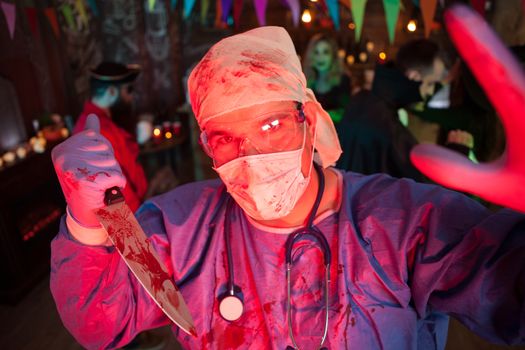 Creepy doctor with his covered holing a kinfe with blood and loo