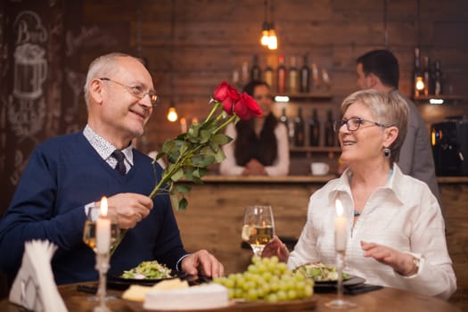 Husband in his sixties giving roses to his wife in a restaurant