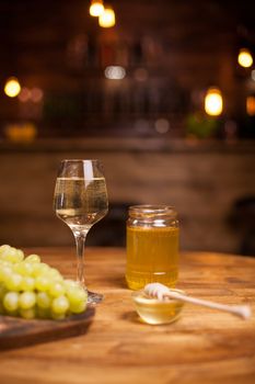 Golden honey jar next to a refined glass of white wine over a rustic table in a vintage pub