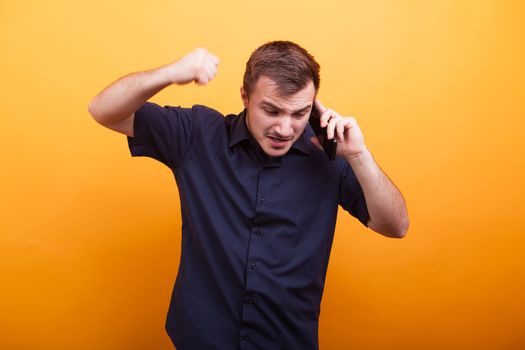 Young man in rage talking on mobile phone over yellow background