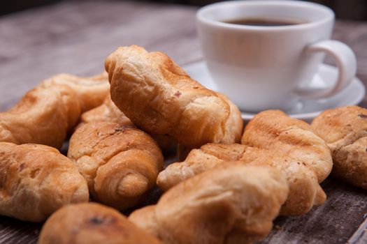 Freshly baked croissants on rustic wooden table with cup of coffee