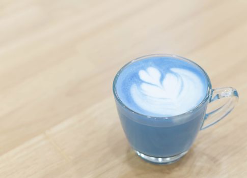 Closeup glass of blue milk with latte art tulip shape on wood ta