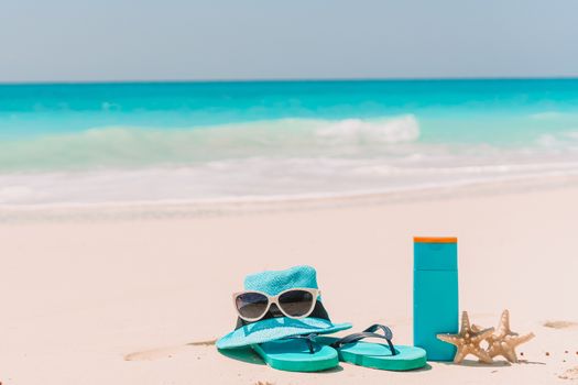 Suncream bottles, sunglasses, flip flop on white sand background ocean