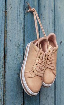  pair of beige fashionable female sports shoes hanging on a cord on a background of a blue old wooden wall, close up