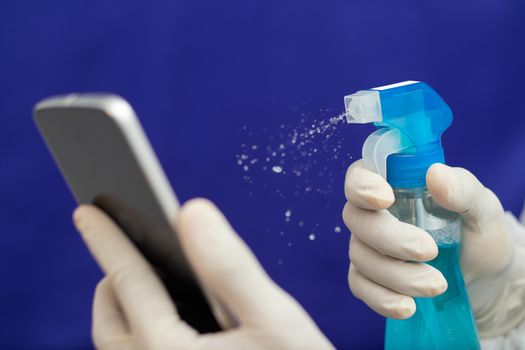 Doctor Cleaning mobile phone to eliminate Covid-19 - Nurse hands with gloves cleaning the phone by liquid sanitizer at hospital - alcohol to wipe contaminating with Coronavirus